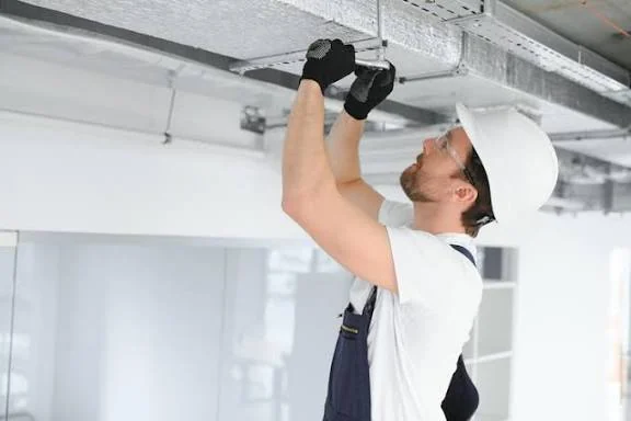 Technician installing overhead metal ductwork