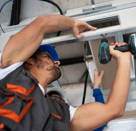 HVAC technician using a cordless drill to service a wall-mounted air conditioner